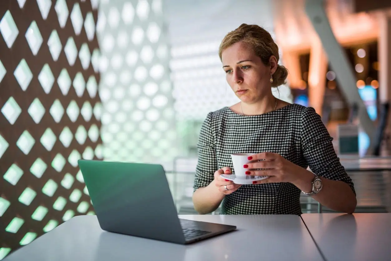 A woman sitting at a table with a laptop and cup.